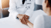 A doctor offering support for a sensitive mold-sick patient, holding hands over the medical exam table.